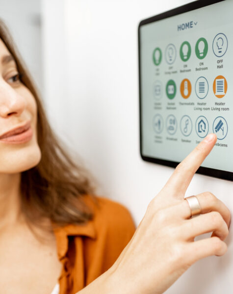 Woman controlling smart devices with a digital tablet at home Young woman controlling home with a digital touch screen panel installed on the wall in the living room. Concept of a smart home and mobile application for managing smart devices at home