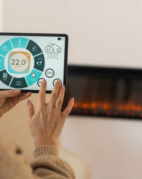 Holding digital tablet in cozy living room with fireplace on background. smart home app Holding digital tablet in cozy living room with fireplace on background. smart home app.